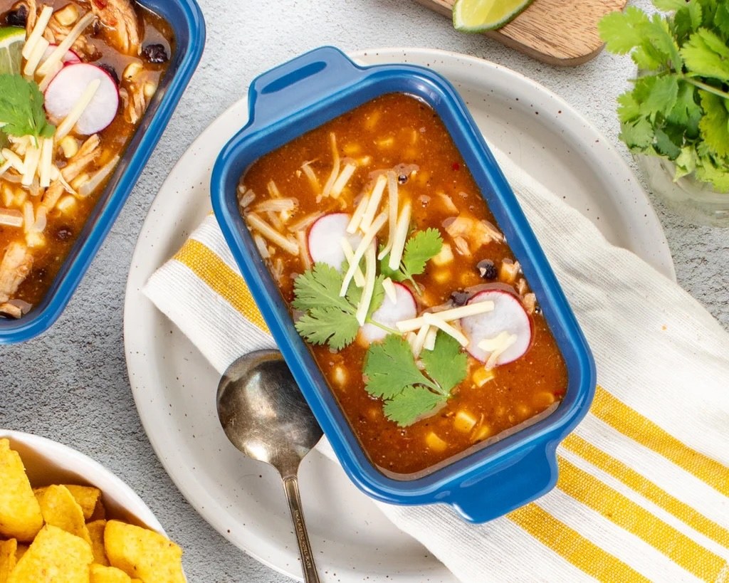Tortilla soup in a blue baking dish, topped with radish, cheese and cilantro